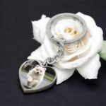 Personalized heart-shaped pet photo keychain in surgical steel, placed on a artificial flower on a black background. Features a custom pet photo engraving on the front with optional custom text engraving on the back. Elegant and sentimental keepsake for pet owners