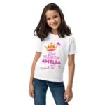 Young girl wearing a white birthday shirt with a gold crown graphic and personalized name on the front