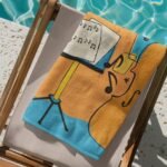 Personalized music towel with custom name, folded neatly on a chair by the poolside, featuring a stylish musical note design – ideal gift for musicians