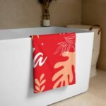 Personalized tropical towel with name for her in alizarin color – draped over a bathtub, showcasing vibrant tropical leaf pattern and custom name design, ideal for spa or home use