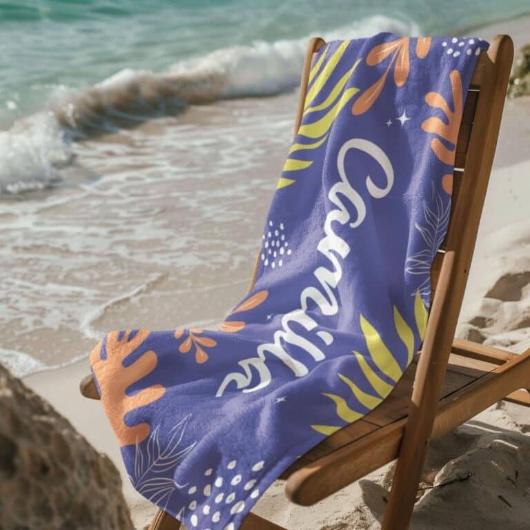 Personalized tropical towel with name for her draped over a wooden chair near the beach – features vibrant tropical leaf design and custom name, ideal for summer vacations or beach getaways